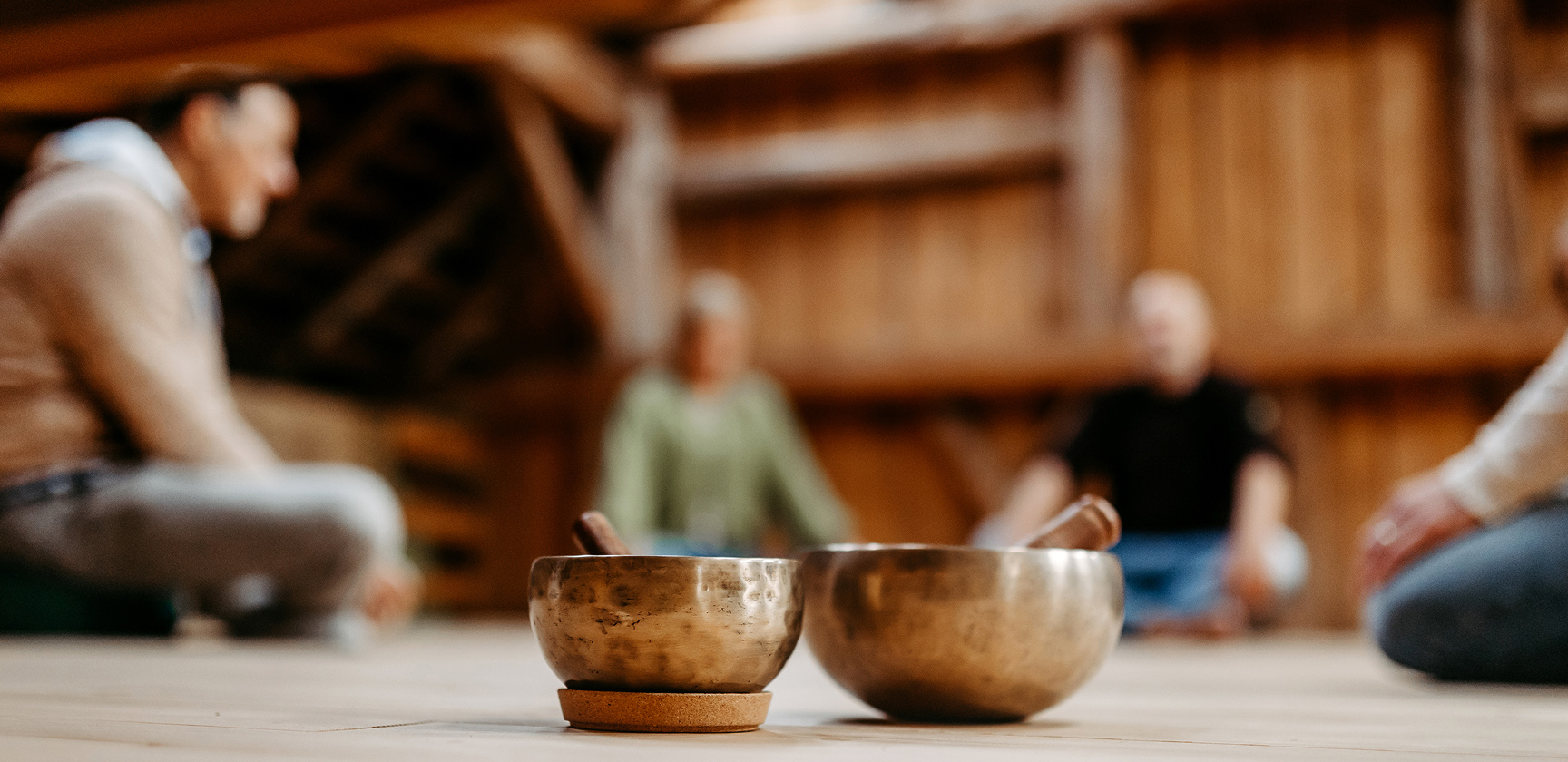 Ein Mann mittleren Alters mit grauem Haar und kurzem Bart blickt nachdenklich in die Ferne, während er im Freien in einer bergigen Landschaft mit Grünflächen und Felsen im Hintergrund steht.